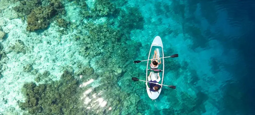 Aerial view of couple kayaking in crystal-clear turquoise waters over coral reefs in the Maldives
