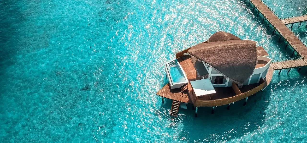 Luxury overwater villa with thatched roof and private deck in crystal clear Maldivian lagoon waters