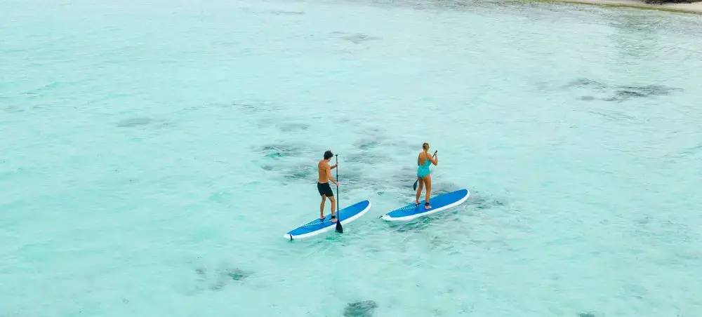 Two travelers paddleboarding on crystal-clear turquoise waters in the Maldives tropical paradise