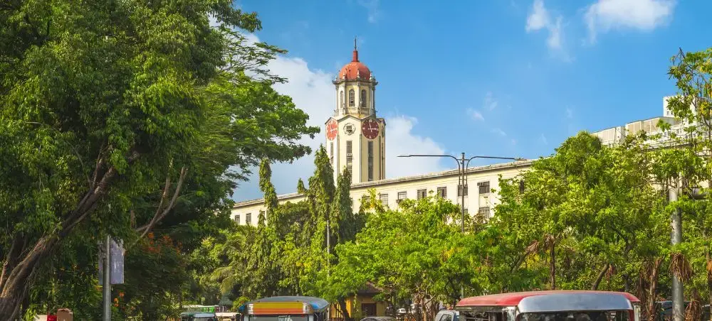 Historic Manila City Hall with distinctive red-domed clock tower surrounded by lush tropical trees