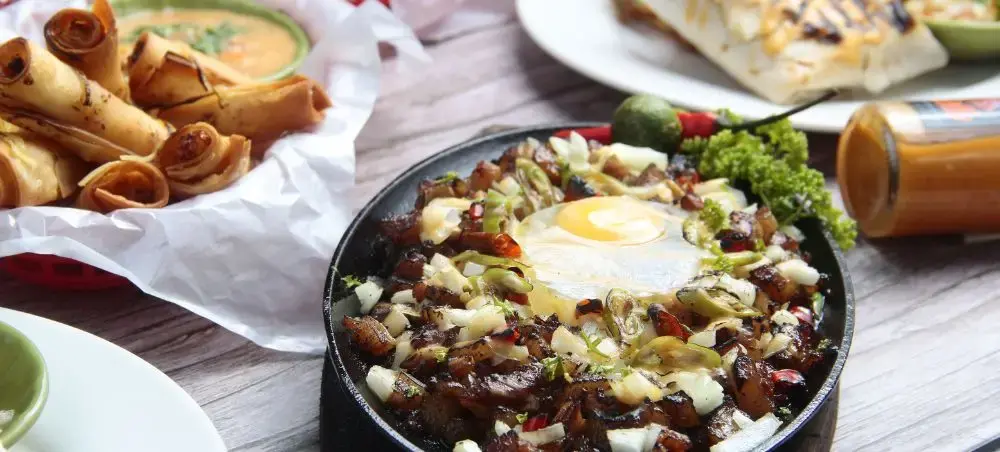 Gourmet Filipino breakfast spread featuring sisig with fried egg and traditional pastries in Manila