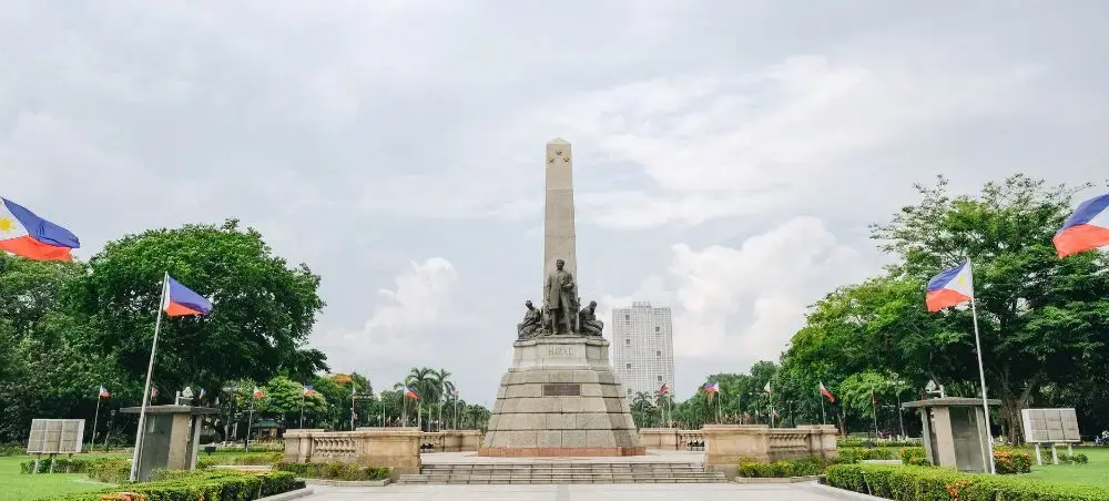 Rizal Monument in Manila's Luneta Park with Philippine flags and modern skyline showcasing the capital city