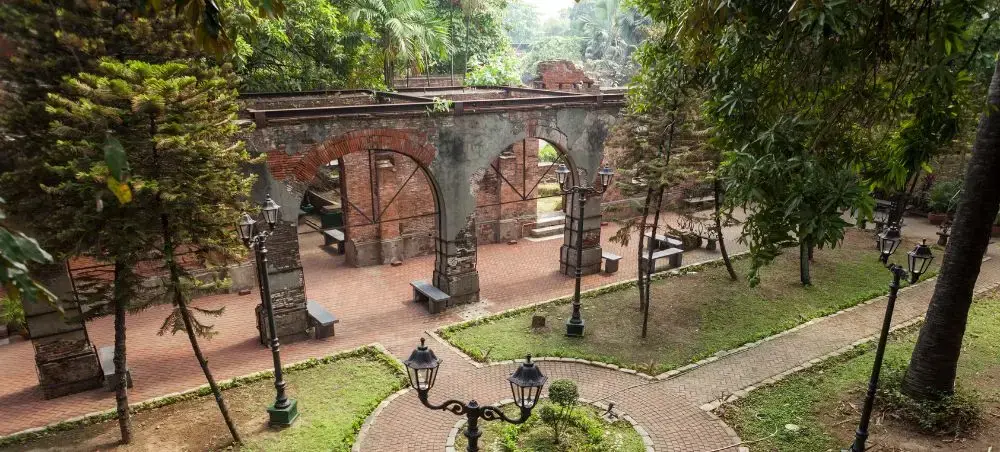 Historic Spanish colonial ruins with brick arches surrounded by lush tropical gardens in Manila, Philippines