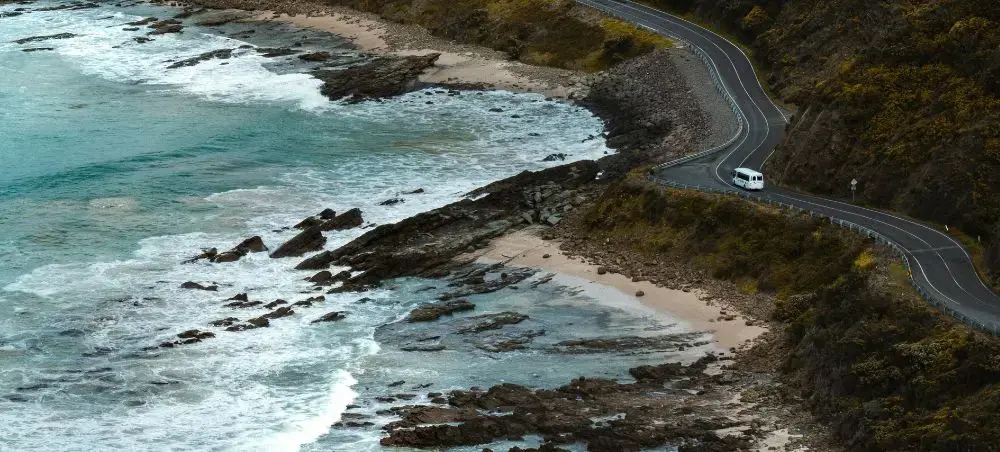 Scenic coastal highway winding along Melbourne's rugged shoreline with turquoise waters and rocky outcrops