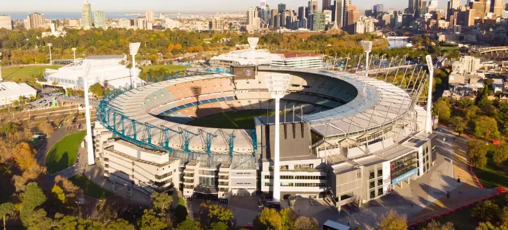 Aerial view of Melbourne Cricket Ground stadium surrounded by parkland with city skyline in background