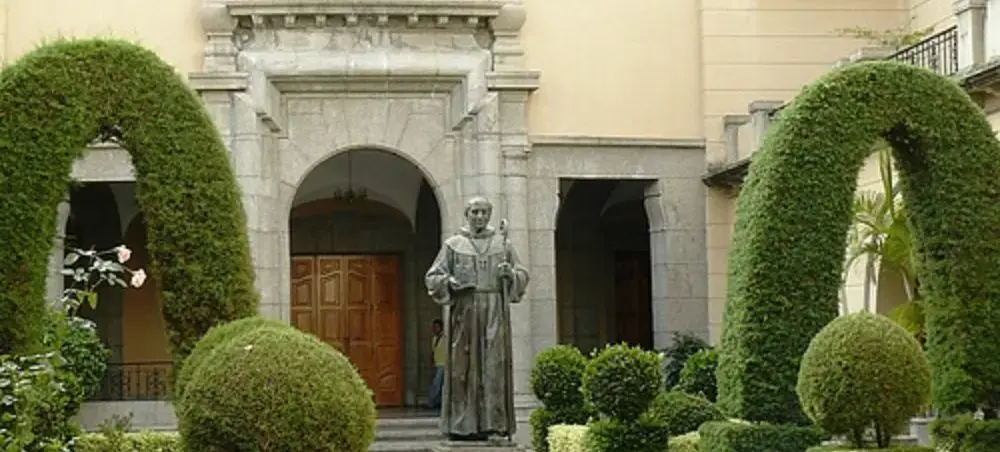 Historic stone archway with manicured topiary gardens and religious statue in Merida, Venezuela