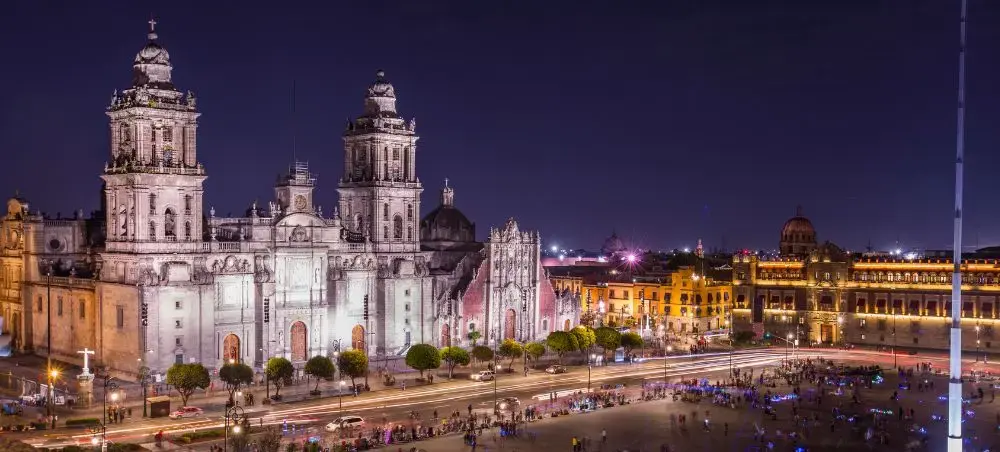 Mexico City Cathedral and Zocalo main square illuminated at night with colonial architecture and bustling crowds