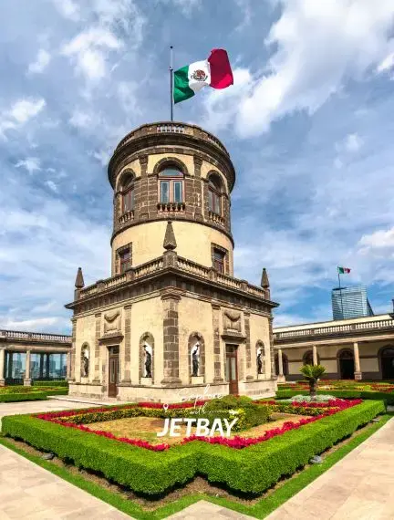 Historic Chapultepec Castle tower with Mexican flag flying above manicured gardens in Mexico City