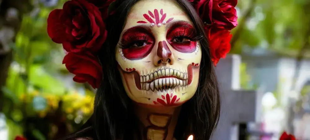 Woman in traditional Day of the Dead makeup with red roses celebrating Día de los Muertos in Mexico City
