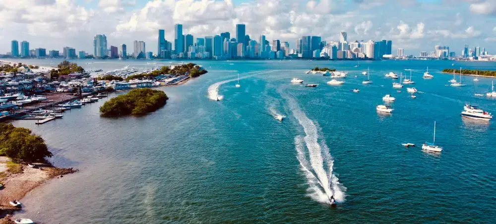 Aerial view of Miami's turquoise bay with luxury yachts and speedboat wake against downtown skyline