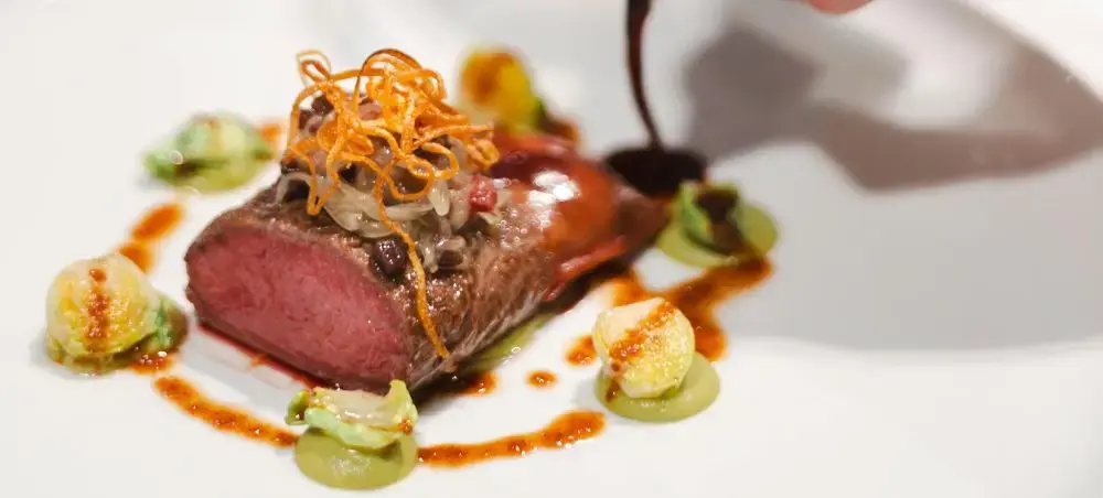 Gourmet seared beef tenderloin with Brussels sprouts and orange garnish showcasing Milan's fine dining scene