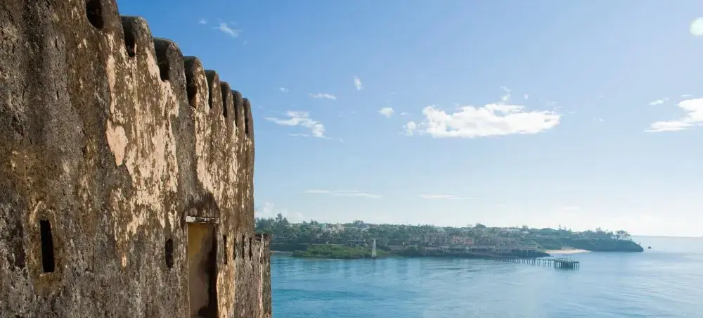 Ancient Fort Jesus walls overlooking turquoise Indian Ocean waters and Mombasa coastline under blue sky