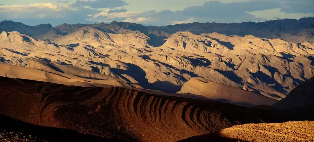 Dramatic golden-hour lighting illuminates Morocco's Atlas Mountains with layered ridges and desert valleys
