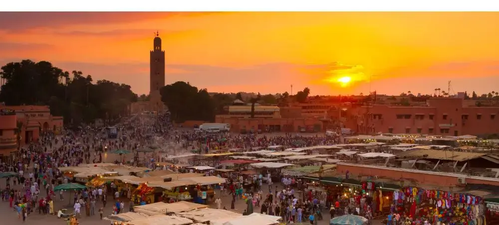 Bustling Marrakech marketplace at golden sunset with Koutoubia Mosque minaret towering over vibrant souks