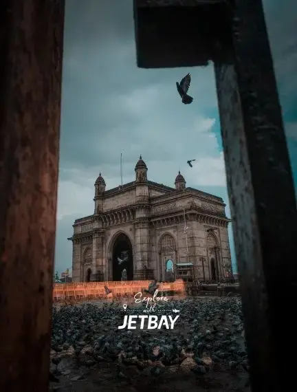 Gateway of India monument in Mumbai framed by stone archway with seagulls flying overhead at dusk