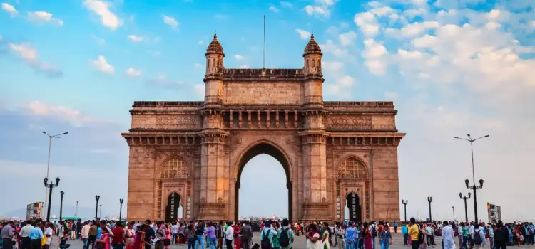 Gateway of India monument in Mumbai with crowds of visitors under dramatic cloudy sky at golden hour