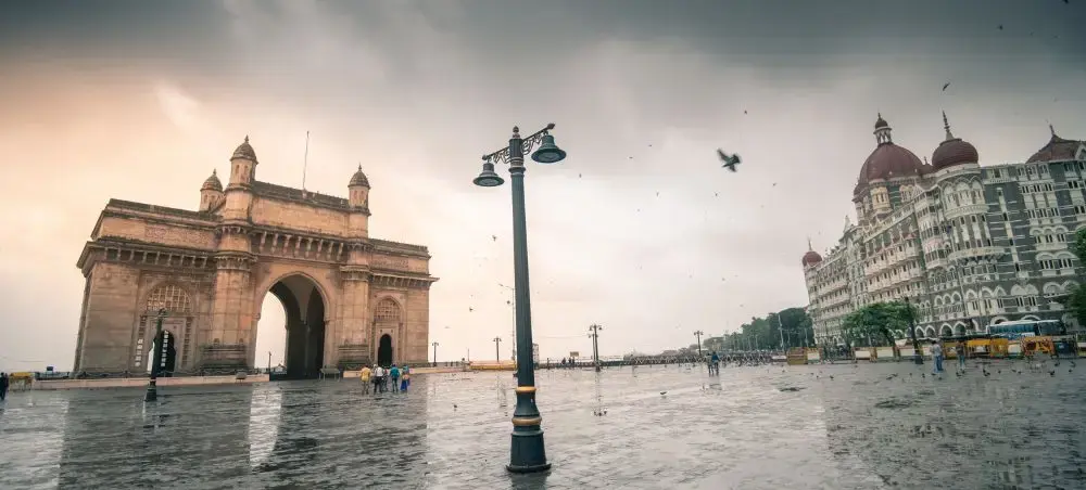 Gateway of India monument and Taj Mahal Palace Hotel overlooking Mumbai's waterfront under dramatic skies