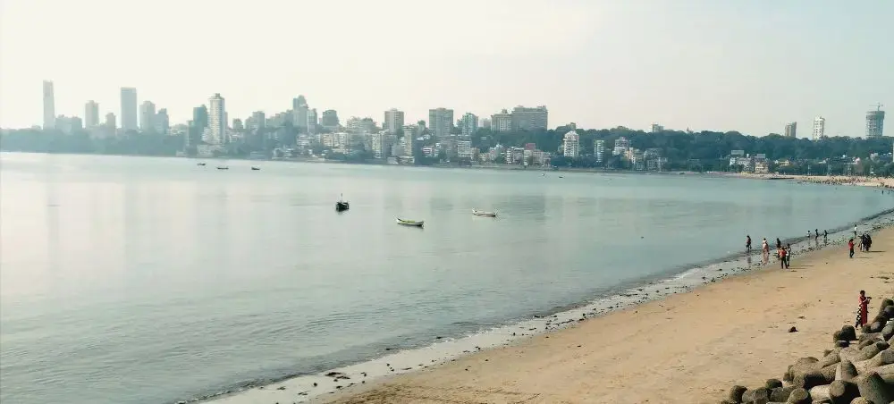 Mumbai's Marine Drive waterfront with city skyline, calm Arabian Sea, and beachgoers enjoying the coastline