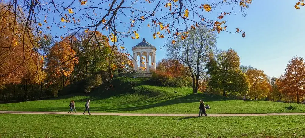 Autumn foliage frames Munich's historic Monopteros temple in Englischer Garten with visitors strolling nearby