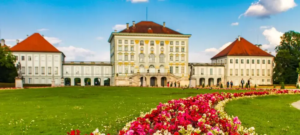 Nymphenburg Palace in Munich with manicured gardens and colorful flower beds under blue sky