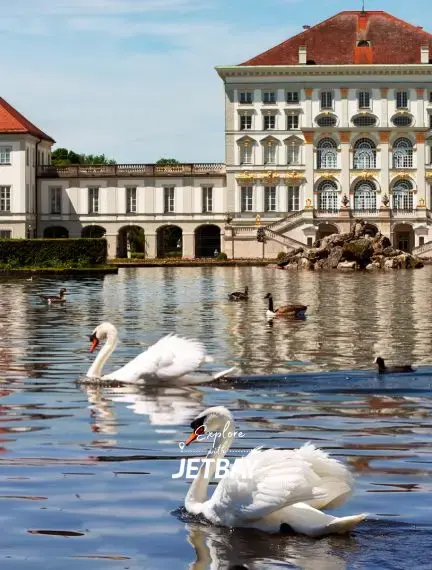 Elegant swans swimming in palace lake with baroque Nymphenburg Palace architecture in Munich, Germany