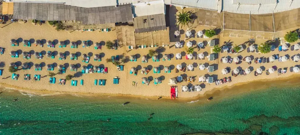 Aerial view of pristine Mykonos beach with turquoise waters, golden sand, and organized umbrellas