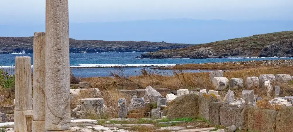 Ancient marble columns and ruins overlooking turquoise Aegean waters on Mykonos, showcasing Greek heritage