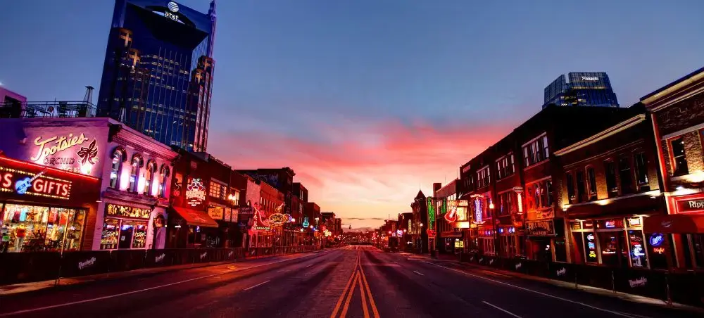 Nashville's iconic Broadway street at sunset with neon-lit honky-tonk bars and downtown skyline