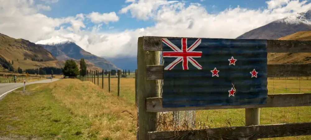 New Zealand flag painted on wooden fence with dramatic mountain landscape and rural countryside