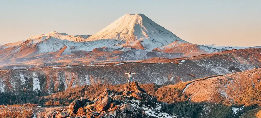 Snow-capped volcanic peaks bathed in golden sunrise light showcase New Zealand's dramatic alpine landscape