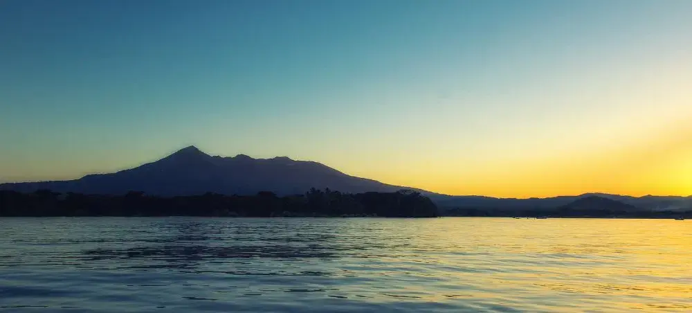 Tranquil lake waters reflecting golden sunset with silhouetted mountains showcasing Nicaragua's natural beauty