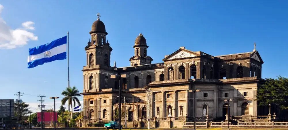 Historic cathedral with twin bell towers and Nicaraguan flag in Managua's central plaza under blue sky