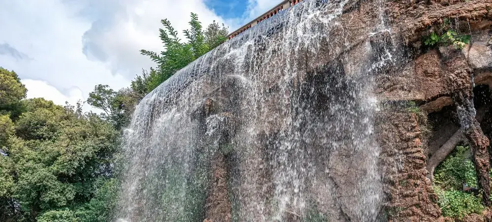 Cascading waterfall flowing over ancient stone architecture surrounded by lush greenery in Nice, France