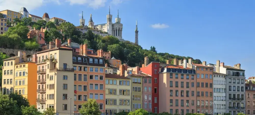 Colorful historic buildings cascade down hillside in Nice with Basilica Notre-Dame visible atop Fourvière Hill