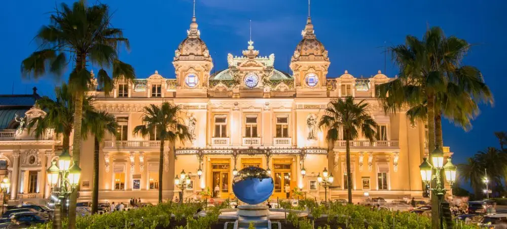 Monte Carlo Casino illuminated at twilight with palm trees and elegant architecture in Monaco near Nice