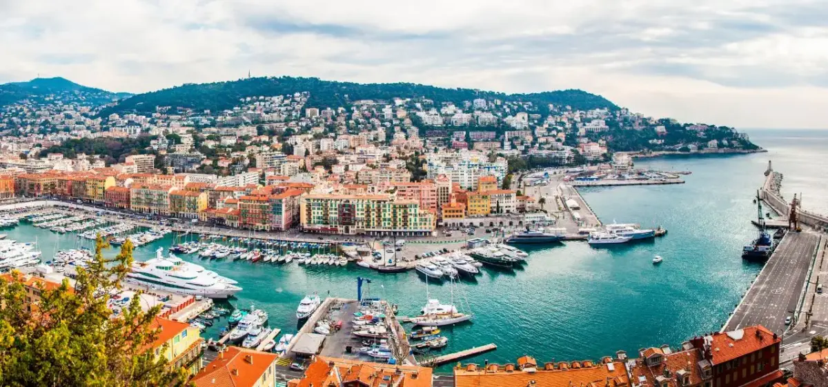 Panoramic view of Nice's colorful harbor with luxury yachts, Mediterranean coastline, and hillside villas