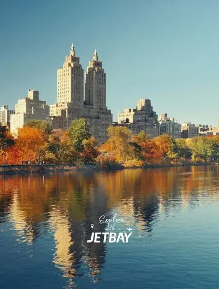 Central Park lake reflecting autumn foliage and Manhattan skyline towers on clear day in New York City