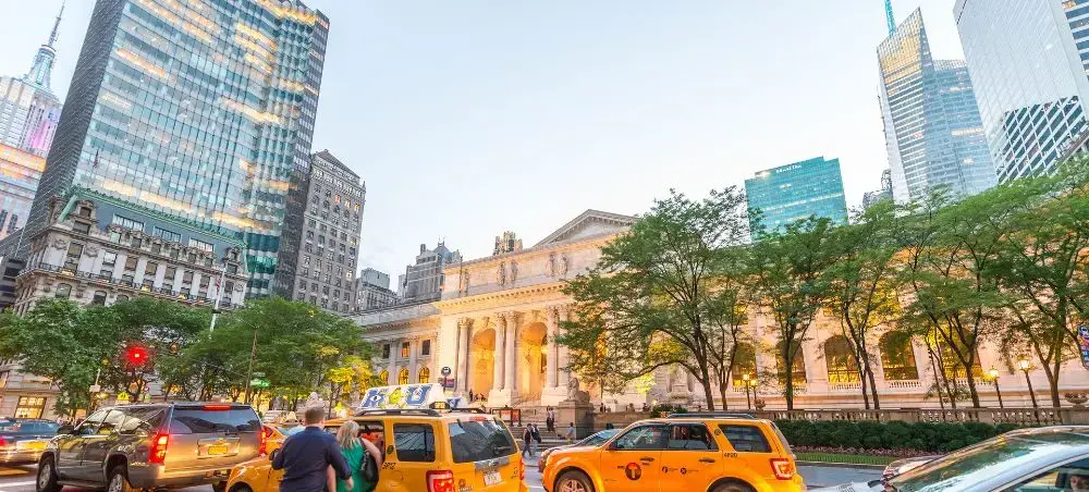 Manhattan skyline with yellow taxis and luxury vehicles near iconic library building at dusk