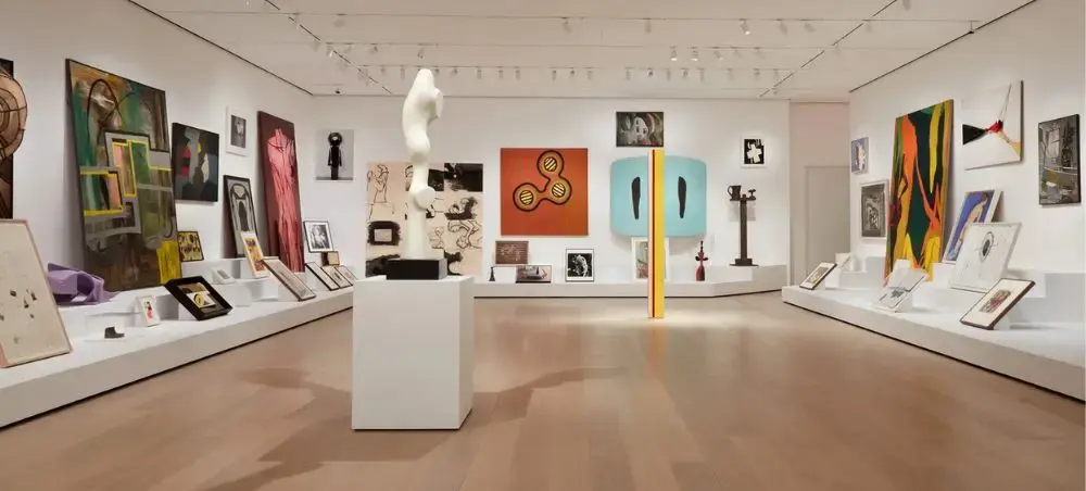 Modern art gallery interior with colorful paintings and sculptures displayed on white walls and pedestals