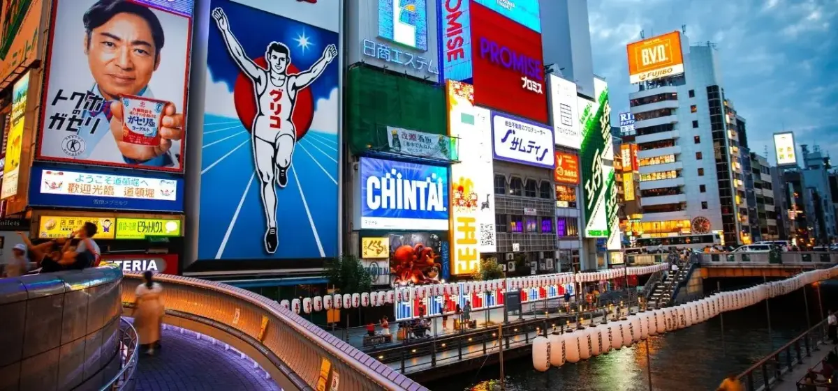Vibrant Osaka cityscape featuring illuminated billboards and traditional lanterns along Dotonbori canal at dusk