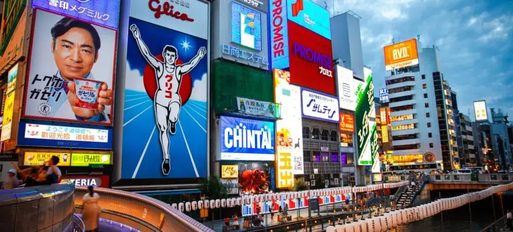 Vibrant neon billboards and digital displays illuminate Osaka's Dotonbori district at dusk for luxury travelers