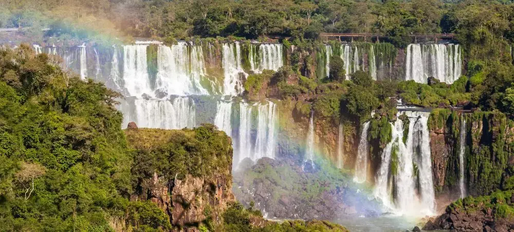 Spectacular Iguazu Falls cascading through lush rainforest with rainbow mist, showcasing Paraguay's natural beauty