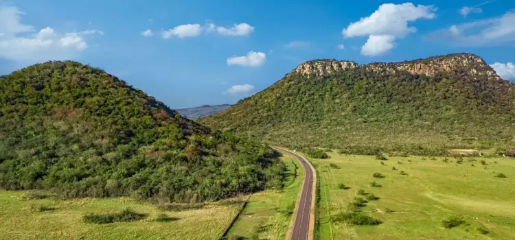 Scenic highway winding through Paraguay's lush green hills and valleys under bright blue sky with clouds