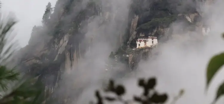 Traditional Bhutanese monastery perched on misty mountain cliffs in Paro, showcasing dramatic Himalayan landscape