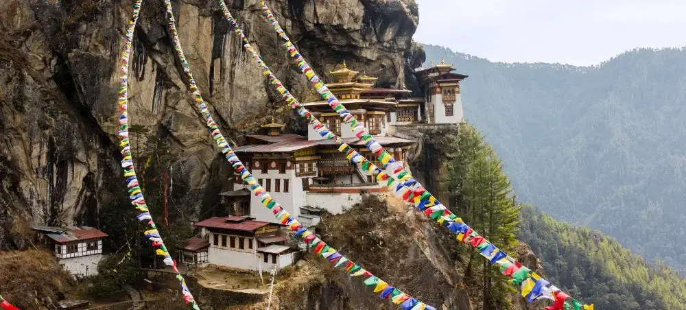 Tiger's Nest Monastery perched on cliff face in Paro valley with colorful prayer flags and Himalayan peaks
