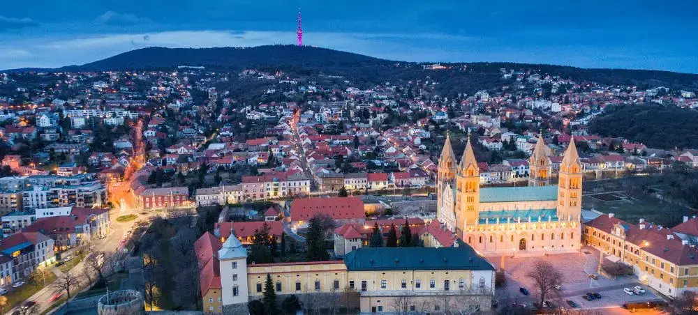 Aerial twilight view of Pecs Cathedral and historic city center illuminated against rolling Hungarian hills