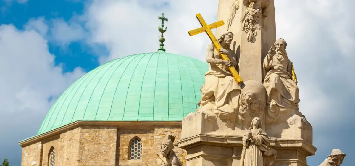 Historic baroque monument with ornate stone sculptures and green copper dome under blue sky in Pecs Hungary