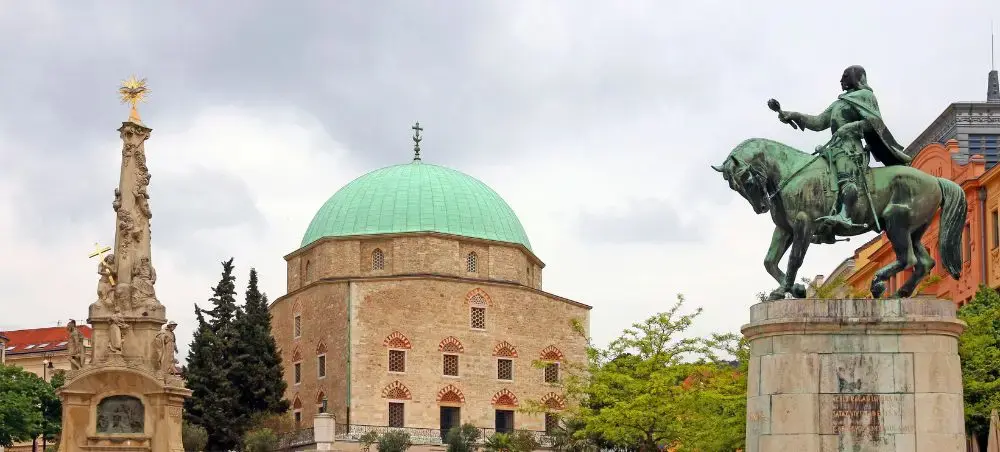 Historic Pecs city center featuring Ottoman-era mosque with green dome and bronze equestrian statue