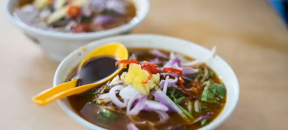 Traditional Penang assam laksa bowls with tamarind broth, fish, vegetables and spicy paste garnish