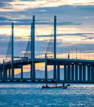 Penang Bridge illuminated at sunset with luxury yacht in foreground showcasing Malaysia's premier destination
